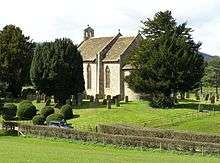 grey stone building set in background with green fields and graveyard in foreground