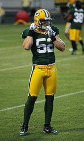 A picture of Clay Matthews III on the filed in uniform adjusting his chin strap.