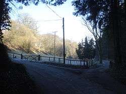 A landscape scene, a wooden mound is to the left.