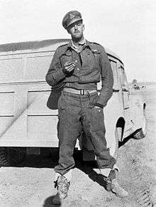 Informal full-length portrait of uniformed man wearing peaked cap and smoking a cigarette