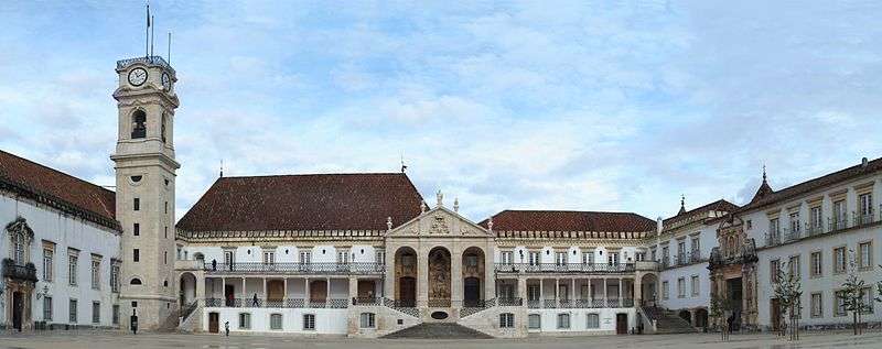 A number of buildings surrounding a central court with a clocktower to the left.