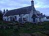 A long, slightly shabby looking chapel, whitewashed with a small belfry. Many different-sized windows are visible.