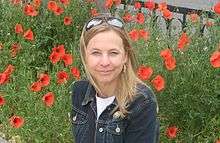 Woman smiling outdoors with flowers in background.