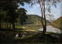 Four people sit together on a shaded lawn beside a riverside path. A small boat sails on the river, which bends away into a gap between sunlit wooded hills.