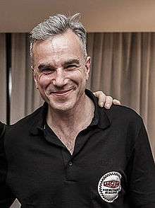 A smiling man with grey hair wearing a black collared shirt.