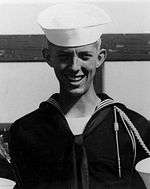 A black and white image of Ray in his military uniform with hat. His head is ducked down slightly and he is smiling at the camera.