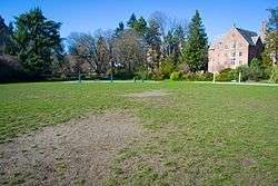 Grass field with trees and buildings at rear