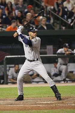 A man preparing to bat on a baseball field. He is wearing a gray jersey and pants and a dark blue batting helmet; the jersey has a blue "NEW YORK" in the front, and the helmet has a white interlocking "N" and "Y" logo.