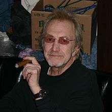 Photograph of Dewey Martin sitting in a chair and smoking a cigar