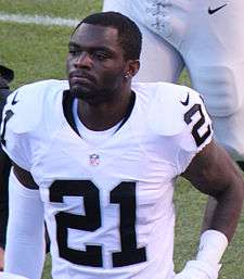 An American football player looks to his right. He is not wearing his helmet. He is wearing a white jersey with the number 21 across his chest in black.