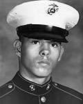 Head of a young Hispanic man wearing a dark military jacket and a white peaked cap with a black visor and an eagle-globe-and-anchor emblem on the front.