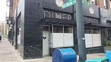 Corner exterior storefront of a building with a black first floor and a drown brick second floor