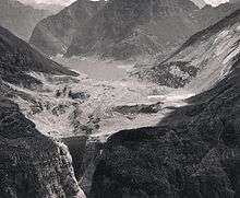 The lake behind the Vajont Dam, surrounded by forested mountains, and mostly filled with mud and debris.