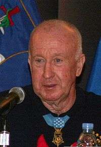 Older bald man wearing black shirt with medal around neck