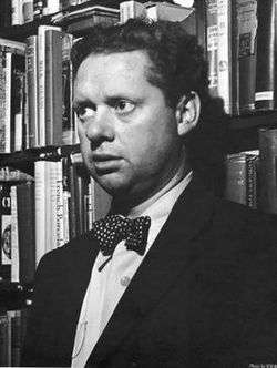 A black and white photo of Thomas in a book shop, he is wearing a suit with a white spotted bow tie.