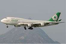 Aircraft in flight. Side view of quad-engine jet with extended landing gear and flaps.