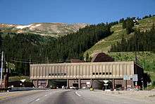 Building facing a large mountain with two openings for the traffic, visible on the roof of the building are large ventilation hoods