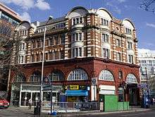 The Bakerloo line entrance, with its classic deep-red faience style arches, with the modern glass-sided and glass-topped flat-roofed extension abutting the original western elevation.