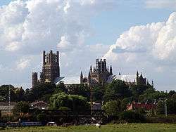 Two towers rise above a stone building on a wooded hill