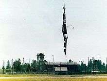 A  B-52 in flight, rolled 90° to the left, very close to the ground and pointing towards it.