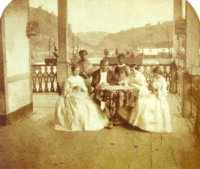 a man and three women seated around a table with two servants standing in the background