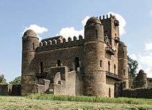 A picture of a four-storey stone castle surrounded by a grassy lawn and four cylindrical towers.