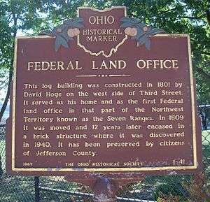 historical marker saying Federal Land Office This log building was constructed in 1801 by David Hoge on the west side of Third Street.  It served as his home and as the first Federal land office in that part of the Northwest Territory known as the Seven Ranges.  In 1809 it was moved, and twelve years later encased in a brick structure where it was discovered in 1940.  It has been preserved by the citizens of Jefferson County.