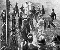 A cricketer leading his team off the field watched by a crowd