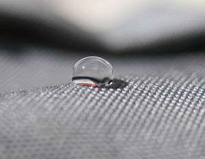 side view of a drop of water on a gray cloth. Looks like about a 120 degree angle.