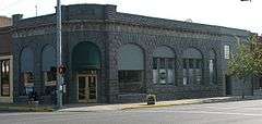 Photograph of a one-story, stone commercial building on a city street corner