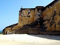 A fortified, but badly-faded yellow-coloured wall looks off into distant sea to the left.