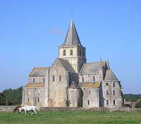  A tall church of grey stone with fine details and a crossing tower topped with a slate-covered spire rises out of rural countryside, where two mares are grazing.