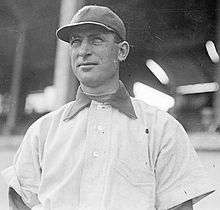 A man in a dark baseball cap facing 3/4 towards the camera.  A baseball stadium grandstand appears to be in the background.