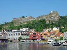 Modest buildings  along the water's edge are guarded by a fortress on the hill above.