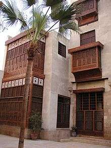 A front view of a large, white building standing behind a thin palm tree.