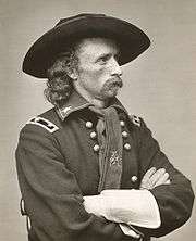 Man with broad hat, scarf, and large gloves in uniform with two columns of buttons