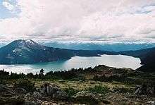 A mountain rising above a lake in the foreground with glaciated mountains in the background.