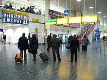 Passengers with luggage looking at arriving-flights board