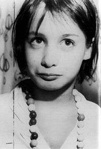 A clearly defined black-and-white close-up photograph of Genie from the chest up against an indeterminate background. Her eyes are focused slightly above and to the right of the camera, and she has an expressionless, vacant, innocent look on her face.