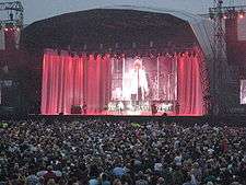 A man, performing on a stage in front of a capacity crowd.