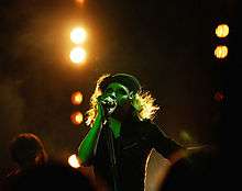 A woman wearing a black hat and shirt singing into a microphone.