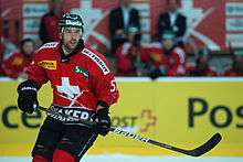 A Caucasian male ice hockey player shown from the knees up. He is wearing a red and white sweater with a dark helmet.