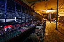 Panels of a manual telephone exchange, with plugs, wires and sockets, receding into the distance