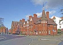 A terrace of red-brick houses with tiled roofs and an octagonal turret at each end.  Each of the houses is different, and include bay windows, different sized gables and dormers.