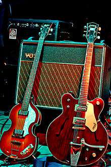 Two electric guitars, a light brown violin-shaped bass and a darker brown guitar, rest against a Vox amplifier.