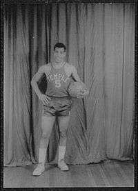 A man, wearing a jersey with a word "TEMPLE" and the number "5" written in the front, is holding a basketball while posing for a photo.