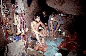 Three people sitting down at an underground camp site surrounded by their equipment