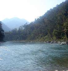 Suspension bridge across a river in a forested mountain landscape.