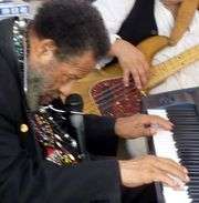 chest high portrait in a black suit playing piano