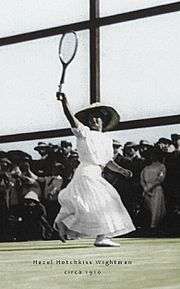 A woman in all white attire is hitting a backhand with the tennis racket in the right hand, which it is a black and white photograph